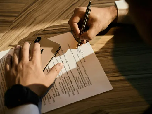 Deux mains au-dessus d’un contrat, sur un bureau de bois éclairé par le soleil