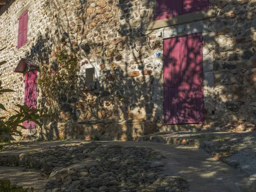Une maison de pierre aux volets rouges, dans la lumière du soir